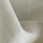 A close-up, detailed shot of a textured off-white or cream linen fabric showing a coarse, natural weave.