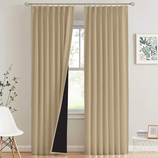 A pair of floor-length beige blackout curtains hanging on a gold rod in a modern living room.