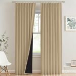 A pair of floor-length beige blackout curtains hanging on a gold rod in a modern living room.