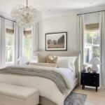 A serene master bedroom with a large upholstered headboard, a bubble-style glass chandelier, and neutral-toned bedding and decor.