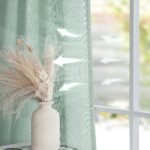 Close-up of breathable green fabric curtains next to a vase with dried pampas grass.
