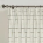 Close-up of pleated white and beige grid curtains hanging on a metallic rod with rings.