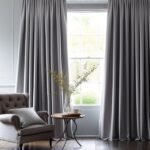 Full-length silver-grey drapes with deep folds framing a window in a classic, elegant interior.