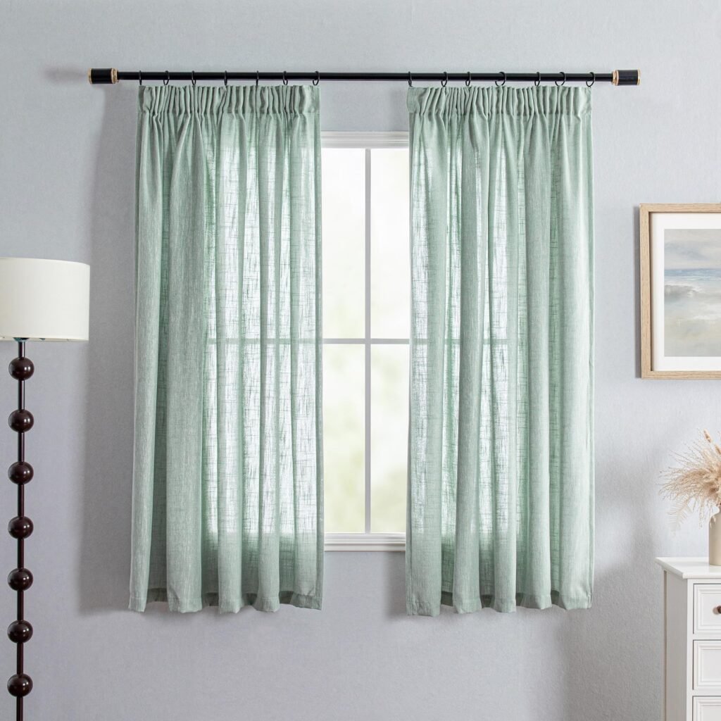Sage green linen-textured curtains hanging on a black rod over a window in a gray room.