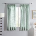 Sage green linen-textured curtains hanging on a black rod over a window in a gray room.